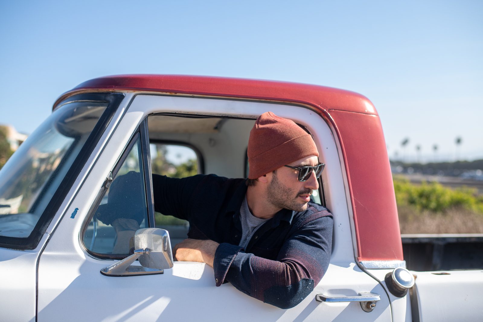 Man wearing rust colored Rora Basics beanie, leaning out a vintage truck window