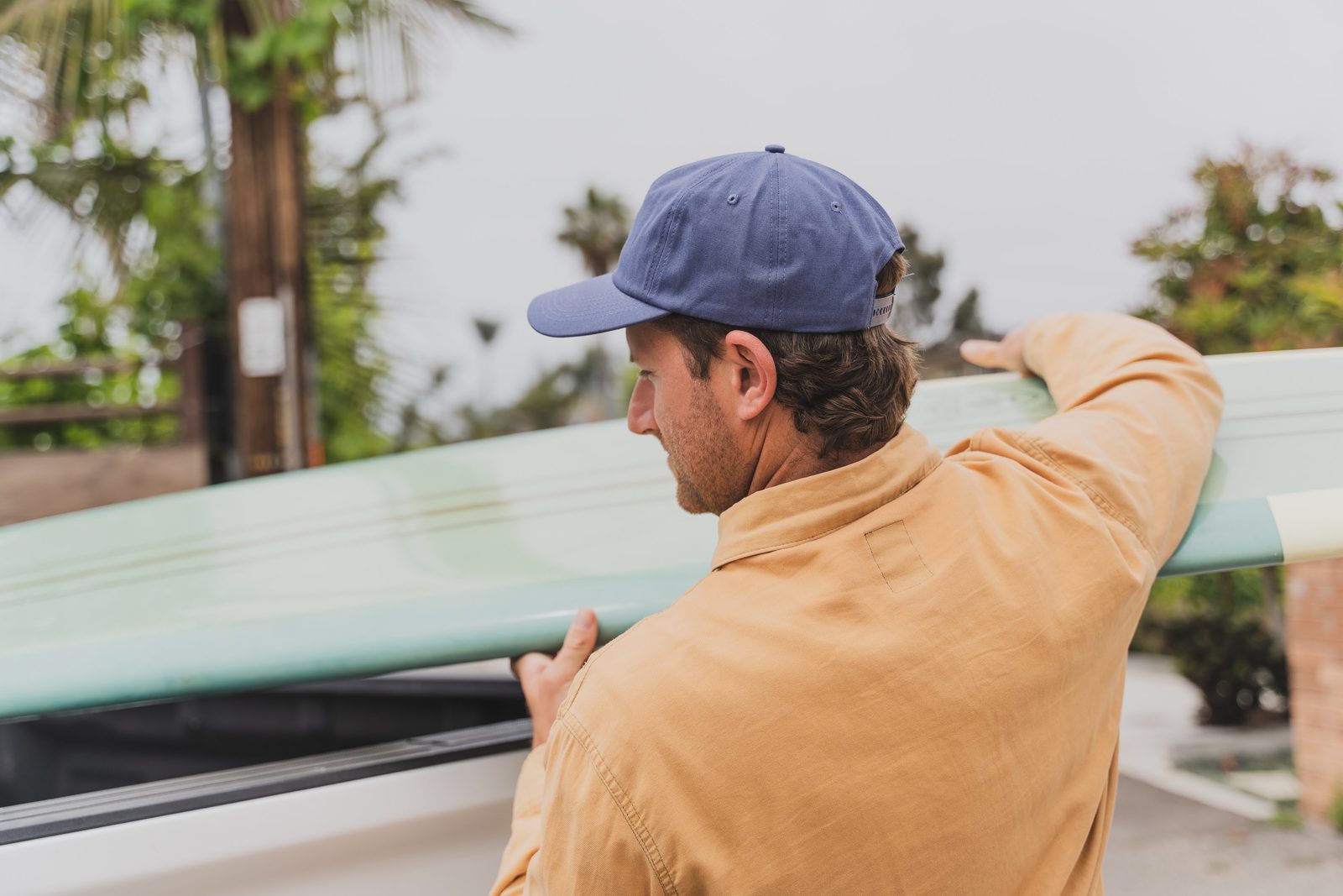 Man wearing navy Rora Basics cap carrying a surfboard